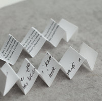 a series of white paper notes or cards with handwritten messages on them, arranged in a zigzag pattern on a gray surface.