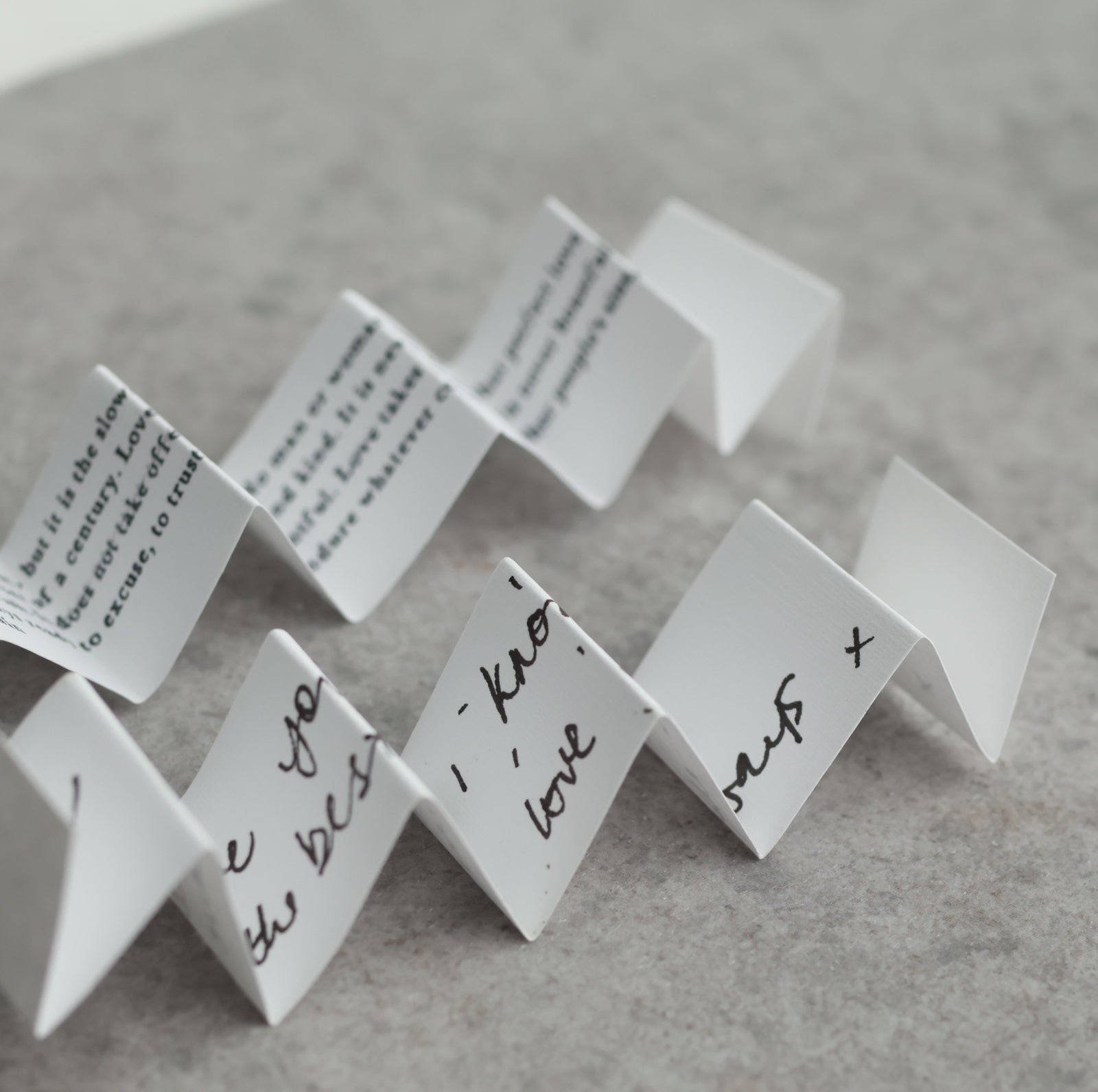a series of white paper notes or cards with handwritten messages on them, arranged in a zigzag pattern on a gray surface.