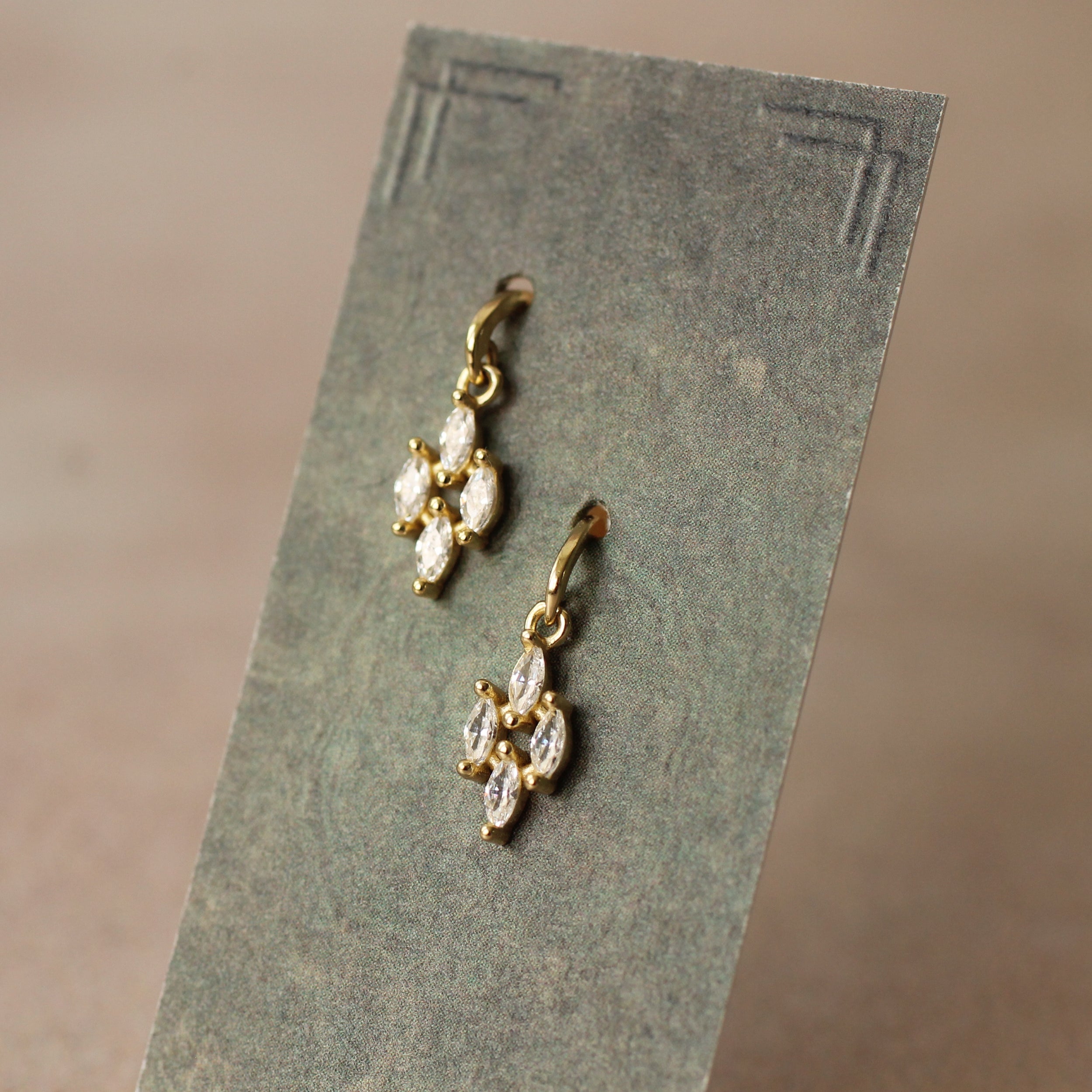 a pair of gold earrings with clear gemstones, displayed on a gray card or paper.