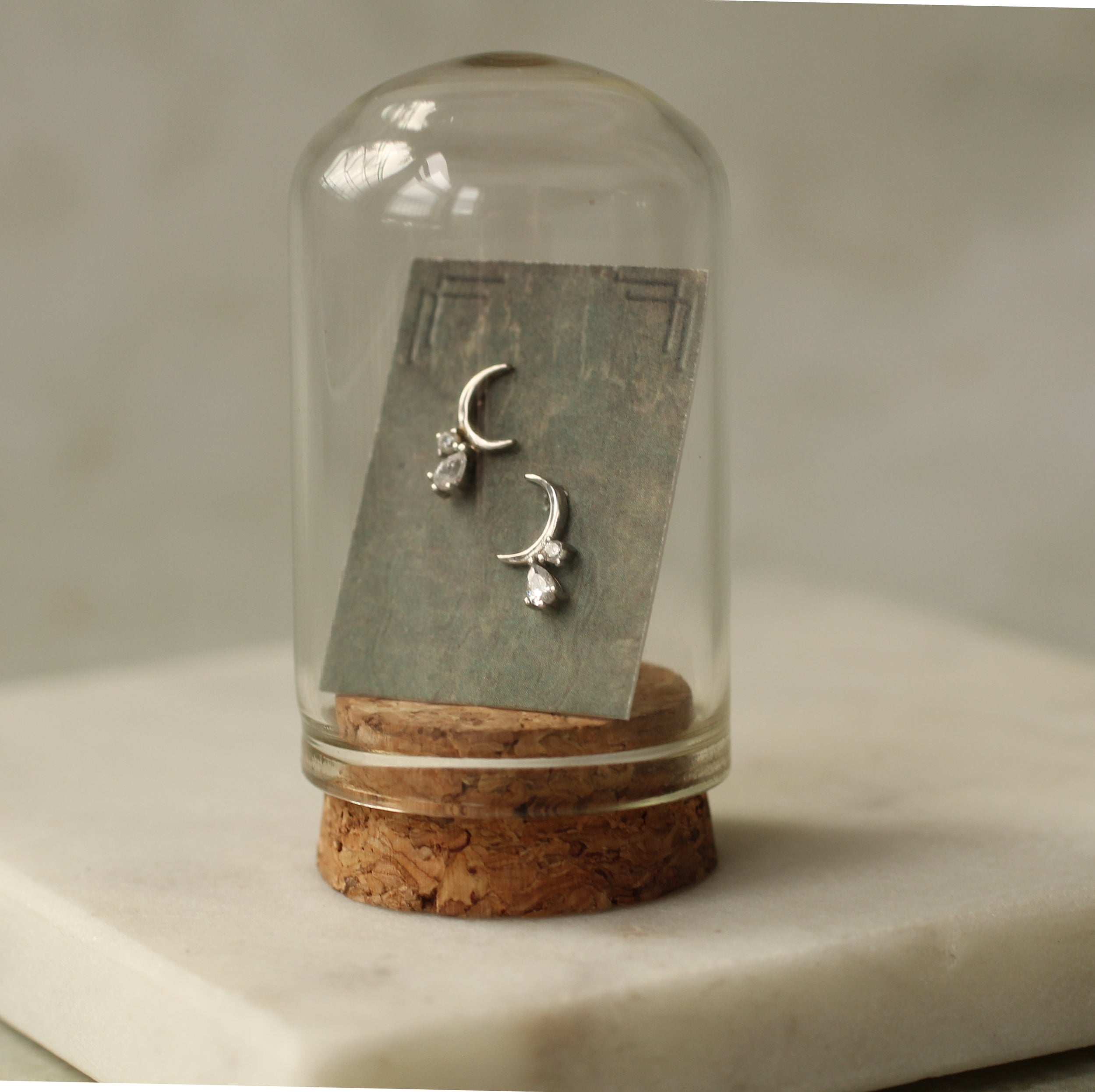 A pair of silver earrings with a cork base and a glass display case containing the earrings.