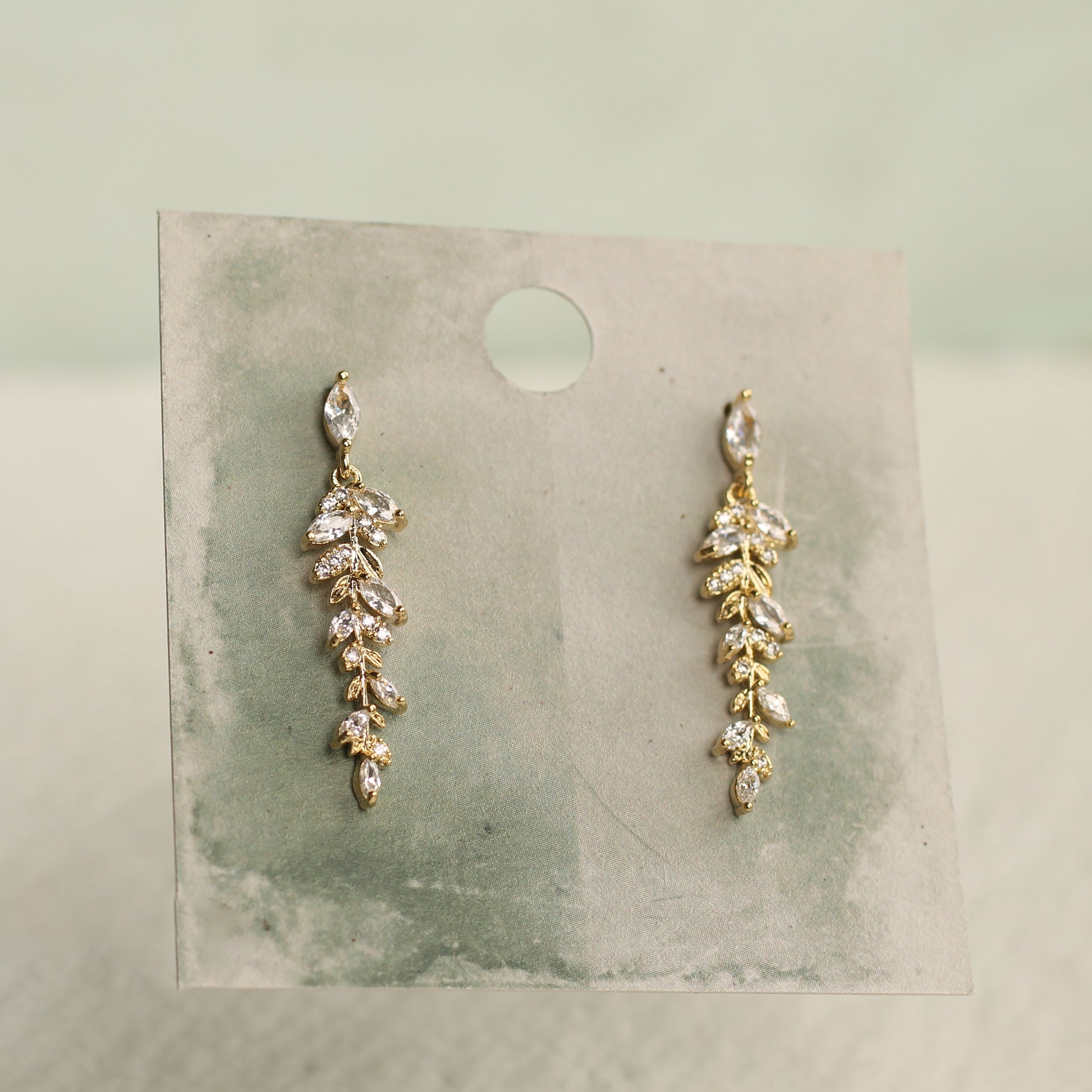 A pair of gold earrings with small, clear stones hanging from a thin, elongated branch-like design.