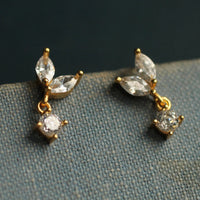 A pair of gold earrings with clear gemstones, including a large diamond and smaller diamonds, hanging from the ear hooks.