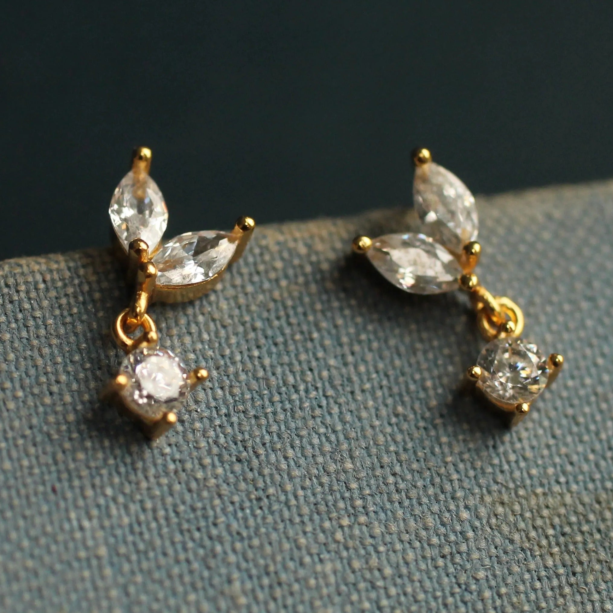 A pair of gold earrings with clear gemstones, including a large diamond and smaller diamonds, hanging from the ear hooks.