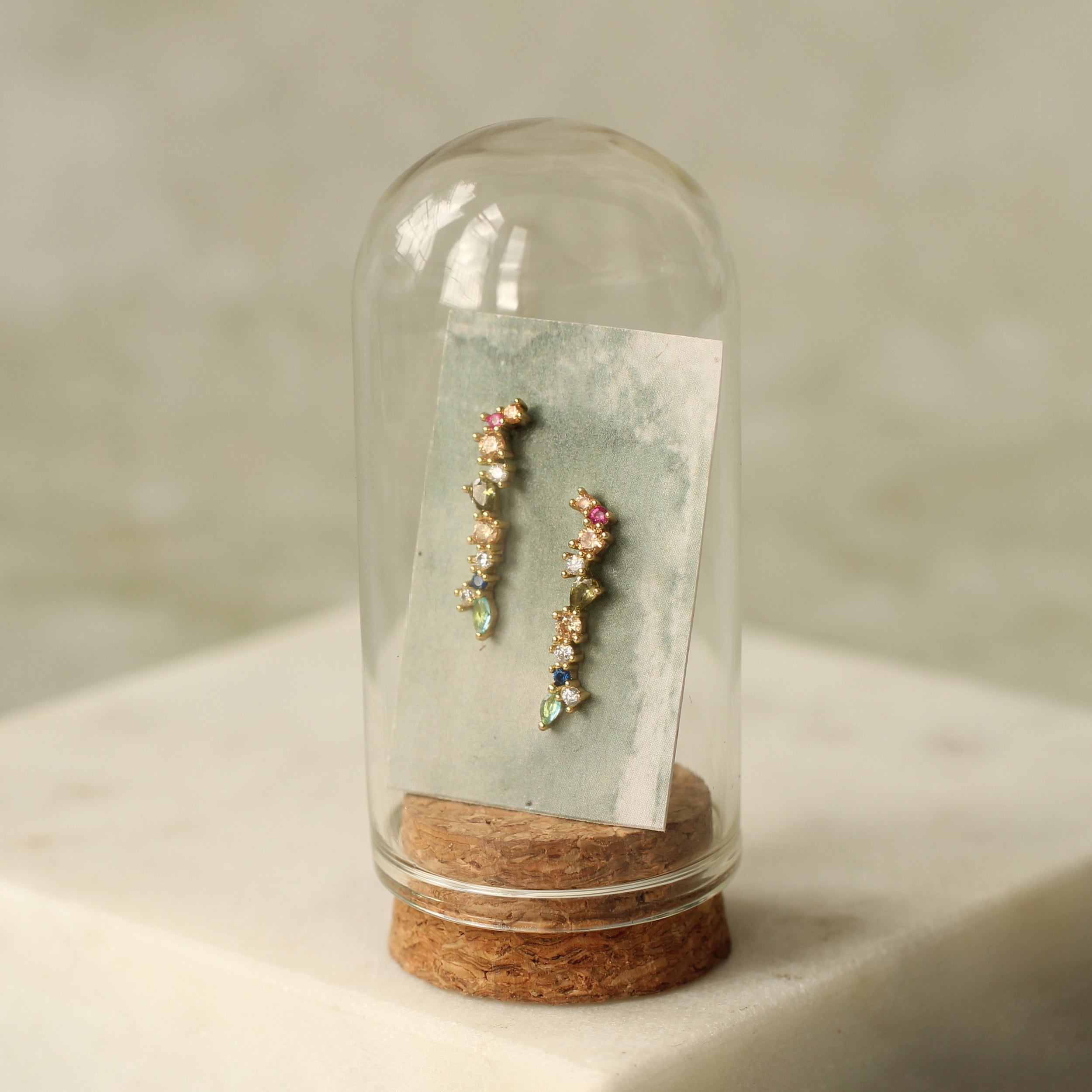 A pair of earrings is displayed in a glass dome, with a piece of paper or card inside the dome.
