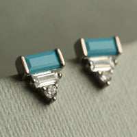 A pair of earrings with blue gemstones and silver accents, resting on a textured surface.