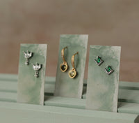 Three small earrings are displayed on green card holders, each with a unique design and color.