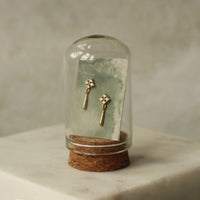 A pair of gold earrings with small diamonds is displayed in a glass case, with a green paper card inside the glass case.