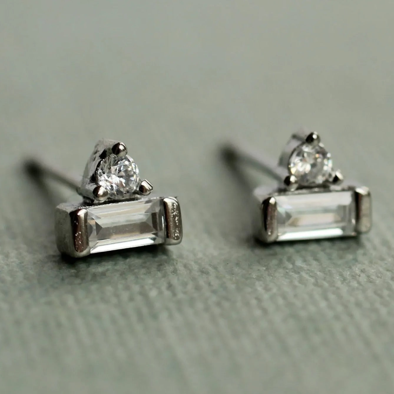 A pair of silver earrings with clear gemstones, resting on a textured surface.