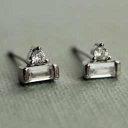 A pair of silver earrings with clear gemstones, resting on a textured surface.