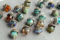 a collection of colorful glass beads and metal acorn-shaped charms arranged on a gray surface.