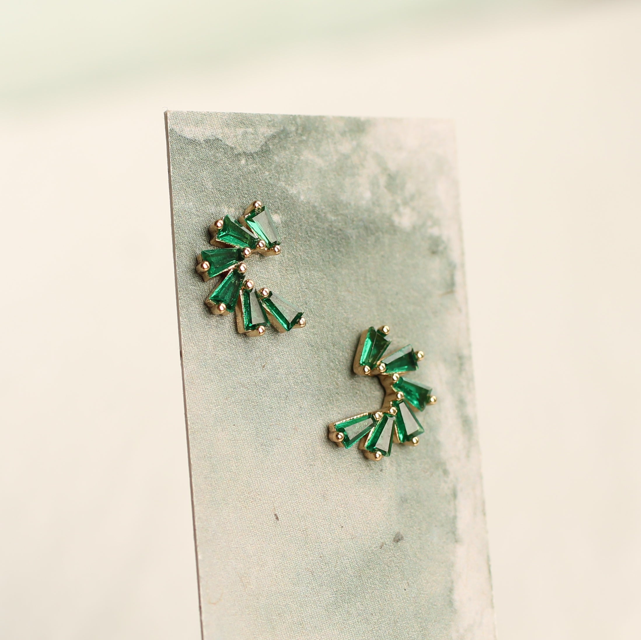 two pieces of earrings with green gemstones, displayed on a grey background.