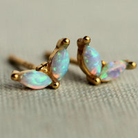 A pair of gold earrings with opal stones, resting on a textured surface.