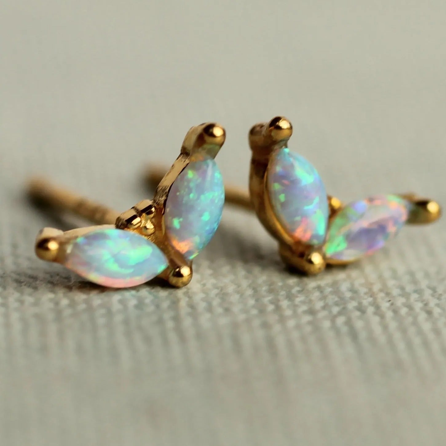 A pair of gold earrings with opal stones, resting on a textured surface.