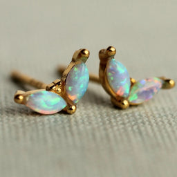 A pair of gold earrings with opal stones, resting on a textured surface.