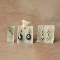 Three pairs of earrings displayed on white cards against a beige background.